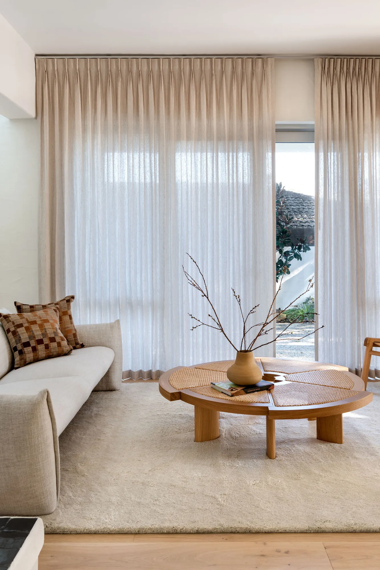 Living room design in a Claremont Perth home by Collected Interiors, featuring linen sheer curtains, a neutral sofa, and a round timber and cane coffee table.